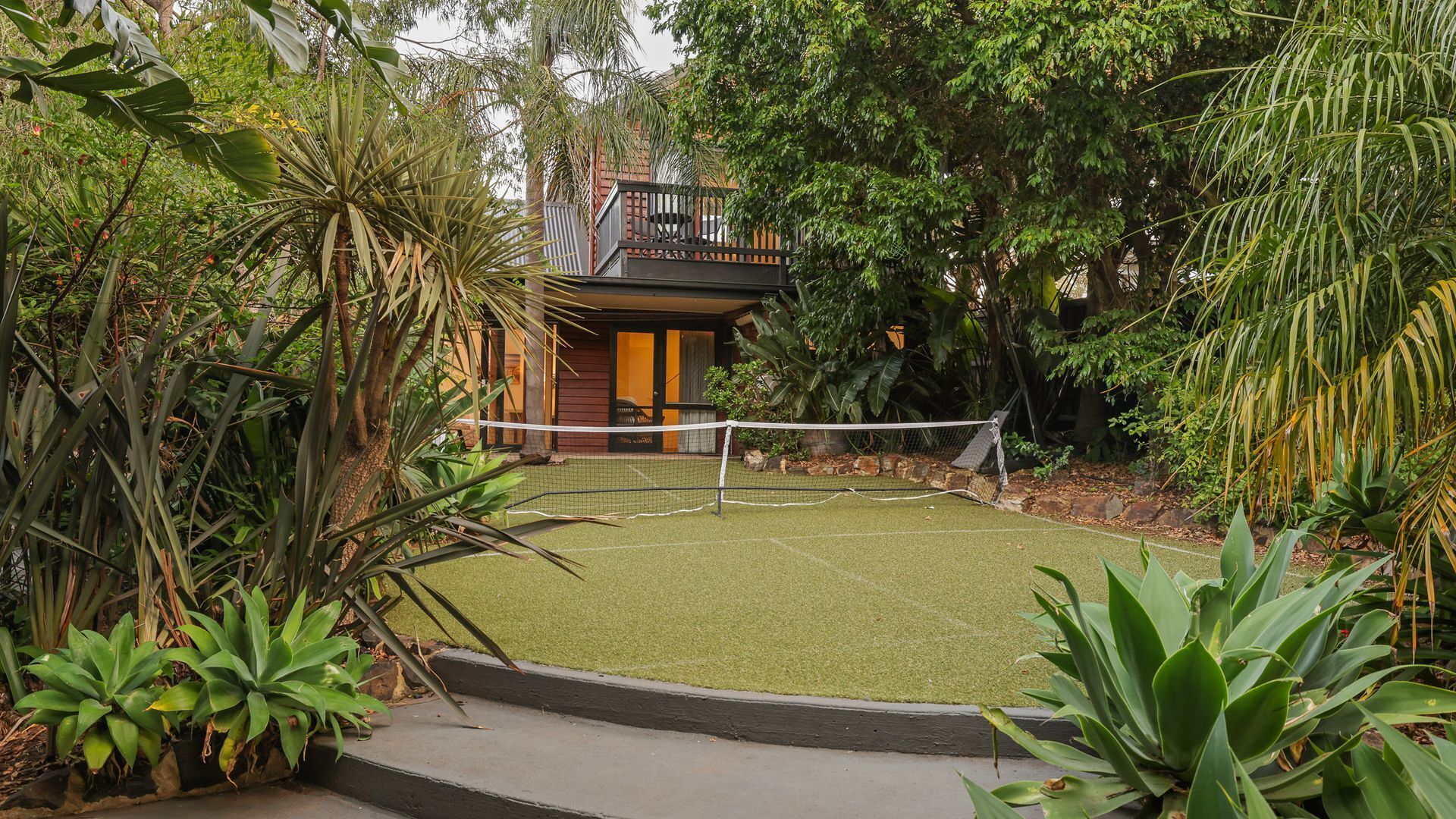 A tennis court surrounded by lush greenery and a wooden building.