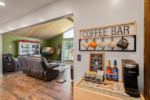 Ein Wohnzimmer mit einer Eckcouch, einer Kaffeestation mit Tassen und Torani-Sirup sowie einer Keurig-Kaffeemaschine.