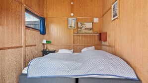 Una habitación con paneles de madera, una cama, una mesita de noche, una lámpara y dos cuadros en la pared.