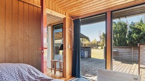 Un dormitorio con techo de madera, una cama con manta estampada, una laptop en el suelo y una puerta corrediza de vidrio que da a una terraza exterior.