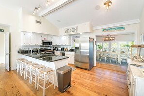 Une cuisine moderne avec des meubles blancs, un réfrigérateur en acier inoxydable et un coin bar équipé de tabourets.