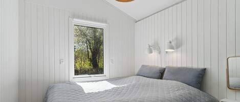 A bedroom with a large bed, a window with a view of trees, a wall-mounted lamp, and a ceiling light.