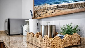 Un comptoir de cuisine avec un four à micro-ondes, une machine à café, un récipient en acier inoxydable et un panier en osier contenant une plante.
