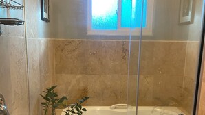 A glass-enclosed shower area with a bathtub, a potted plant, and a window above the tub. - Quaint 1-bedroom bed & breakfast with AC in Los Angeles (Los Angeles)