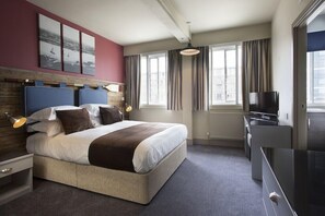 Ein Hotelzimmer mit Bett, Nachttischen, Fernseher und einem Fenster mit Vorhängen.