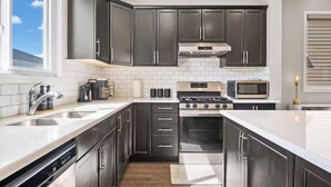 A modern kitchen with dark cabinets, a stainless steel stove, a microwave, and a dishwasher. - 5BR House » King Bed » AC » Pool Table » Garage (Calgary)