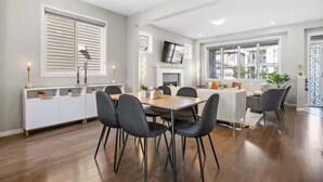 A modern dining area with a wooden table, black chairs, and a white cabinet. - 5BR House » King Bed » AC » Pool Table » Garage (Calgary)