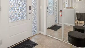 A modern interior with a white door, a glass door with a patterned design, a black bench, and a tiled floor. - 5BR House » King Bed » AC » Pool Table » Garage (Calgary)