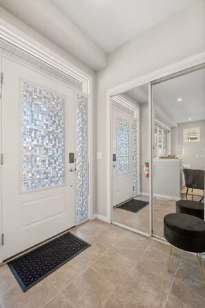 Ein modernes Interieur mit einer weißen Tür, einer Glastür mit Musterung, einer schwarzen Bank und einem Fliesenboden.