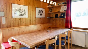 Huoneen sisustus on tehty puusta, ja siellä on pitkä pöytä, tuoleja, taideteoksia seinillä sekä ikkuna, jossa on punainen verho.