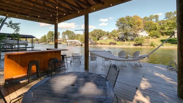 Una terraza de madera con mesa y sillas, una hamaca y un área de bar con vista al lago.