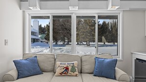 A living room with a beige sofa, two blue cushions, a window with a view of a snowy landscape, and a fireplace.