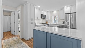 A modern kitchen with white cabinetry, a central island, stainless steel appliances, and a patterned rug.