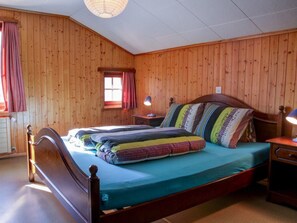 A wooden-paneled bedroom with a single bed, a nightstand, a lamp, and a window with curtains.