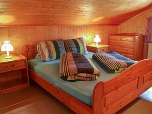 A wooden-paneled room with a bed, two bedside tables with lamps, and a dresser.