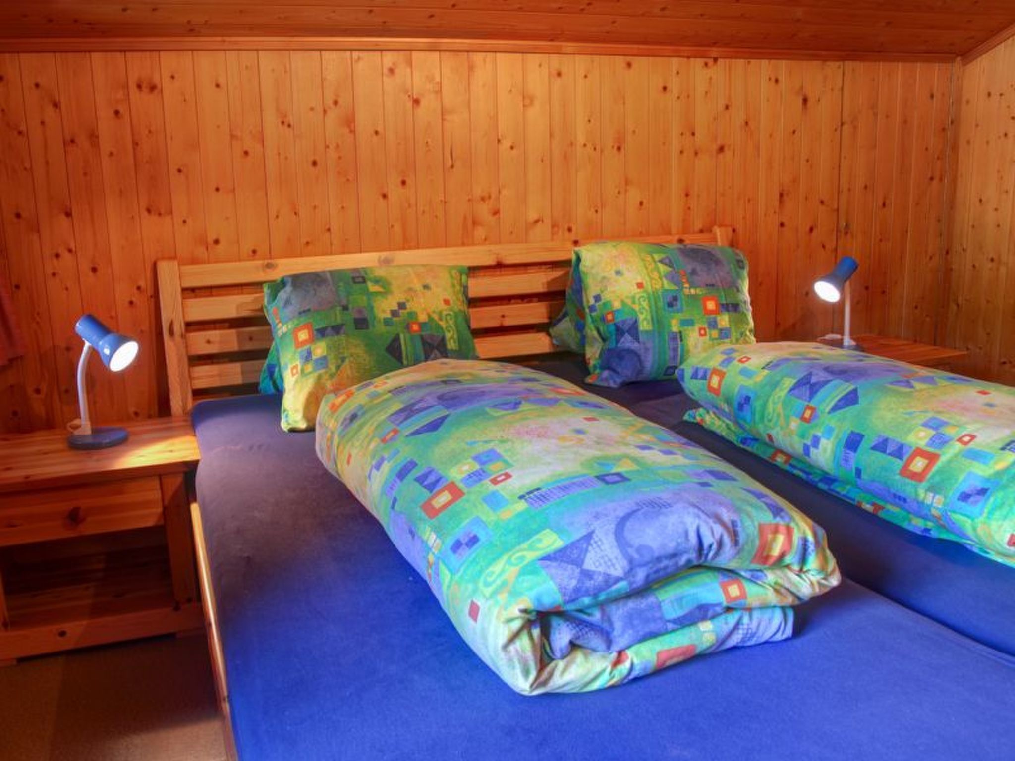 A room with wooden walls and two beds with colorful bedding.