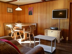 A cozy room with a dining table, chairs, a flat-screen TV, a small cabinet, and a sofa.
