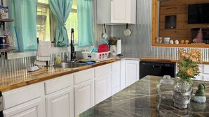 A kitchen with white cabinets, a granite countertop, and a window with teal curtains.