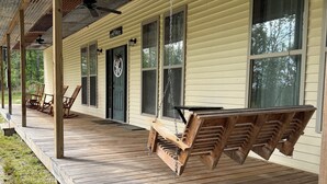 A covered porch with wooden chairs, a swing, and a ceiling fan.