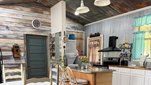A rustic kitchen with a wooden island, a dining area with a table and chairs, and a clock on the wall.
