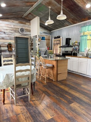 A rustic kitchen with a wooden island, a dining area with a table and chairs, and a clock on the wall. - Unique cabin in Salem Missouri, two bedroom two bath . Built in 2022. (Salem)