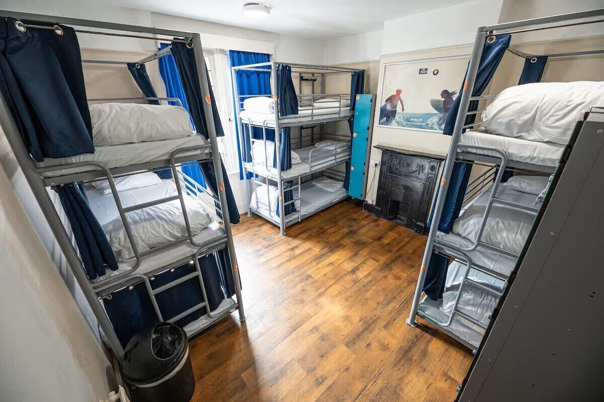 Een slaapkamer met stapelbedden van metaal, een houten vloer en een kleine prullenbak.
