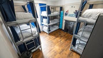 Un dormitorio con literas metálicas, piso de madera y un cesto de basura pequeño.