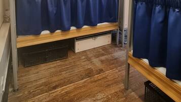 Una cama litera con estructura de madera, un cajón blanco debajo y una cortina azul.