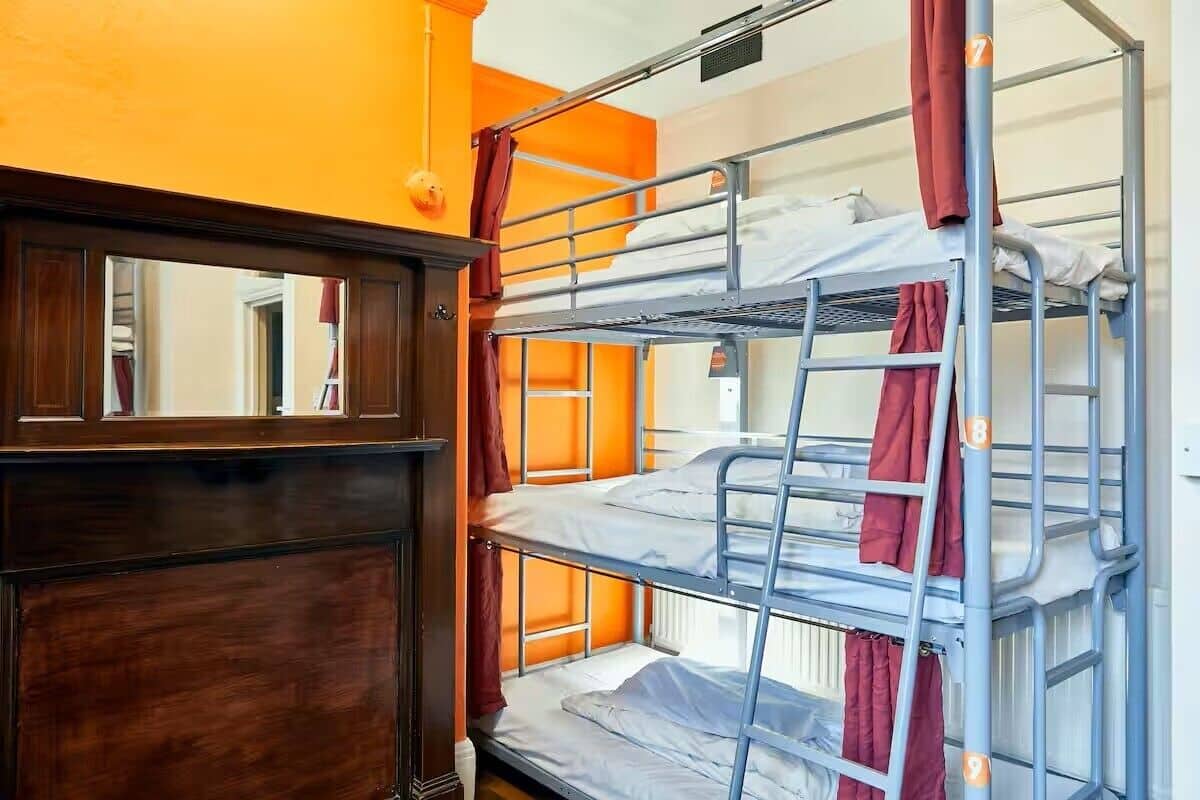 A bunk bed room with orange walls, a wooden wardrobe, and a mirror.