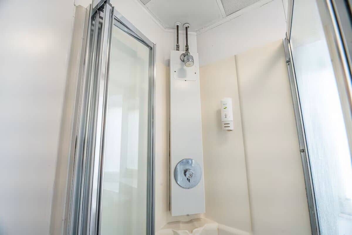 Ducha con puerta de cristal, pared blanca y panel de control.