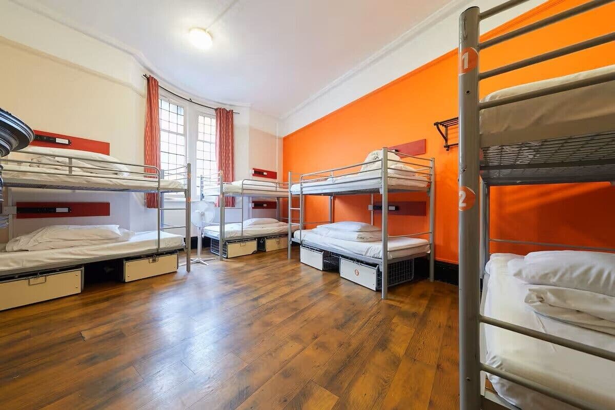 A dormitory room with bunk beds, wooden flooring, and orange walls.