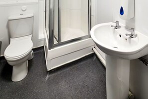 A bathroom with a toilet, a shower with a glass door, and a sink with a mirror. - BacPac Hostel (London)