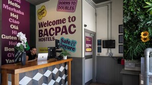 Uma receção com balcão de check-in, um laptop e um sinal de boas-vindas aos hostels BACPAC.