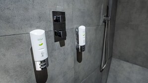 Casa de banho moderna com parede revestida a azulejos cinzentos, chuveiro e dois secadores de mãos fixados na parede.