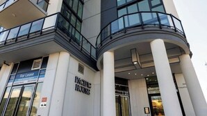 En moderne bygning med et skilt, der siger 'Til leje', skilt med 'PACIFIC HOUSE' og en buet indgang med store søjler.