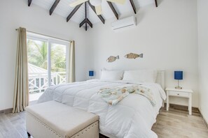 A bedroom with a bed, a nightstand, a bench, and a view of the outside. - Placencia Village Pool, 4 Bed 4 Bath. (Placencia)