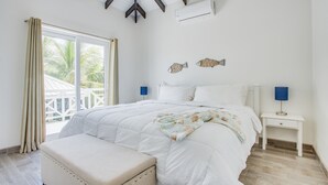 A bedroom with a bed, a nightstand, a bench, and a view of the outside.