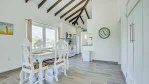 A bright kitchen with white cabinets, a dining table with chairs, and a clock on the wall.