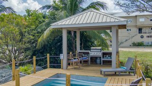 A wooden deck with a pool, lounge chairs, a barbecue area, and a covered pavilion.