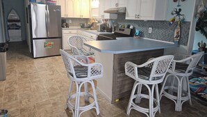 Una cocina con armarios blancos, un refrigerador de acero inoxidable, una isla integrada con taburetes y un salpicadero de azulejos.