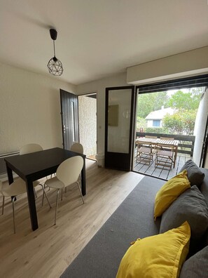 Une pièce comprenant une table à manger, des chaises, un canapé avec des coussins, un luminaire au plafond et une porte-fenêtre coulissante donnant sur un espace extérieur.