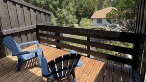 Una terraza de madera con dos sillas Adirondack y vistas a árboles y una casa.
