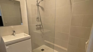 Un baño moderno con ducha de vidrio, un lavamanos blanco y un espejo.