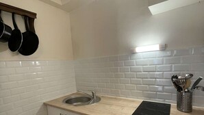 Una cocina con armarios blancos, un fregadero, una estufa y ollas colgantes.
