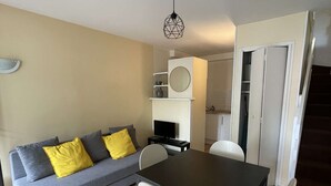 Una sala de estar moderna con un sofá gris, sillas blancas, una mesa de comedor negra y un televisor pequeño.