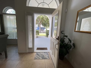 A hallway leading to a door with a view of a residential street, a potted plant, and a tiled floor. - 296 -Relaxing 4-Bedroom Villa with Private Pool, Spa & Games Room (Clermont)