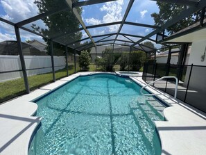 Una piscina cristalina con cerramiento de vidrio, rodeada por una cerca blanca y una zona cubierta.