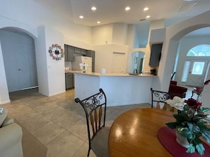 A modern kitchen with a central island, a dining area with a round table, and a living space with a TV. - 296 -Relaxing 4-Bedroom Villa with Private Pool, Spa & Games Room (Clermont)