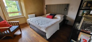 A bedroom with a bed, a radiator, a window, a chair, and a bookshelf. - Saint Pée sur Nivelle, Ancienne labourdine parfaitement rénovée, 10 personnes, piscine (ST PEE SUR NIVELLE)