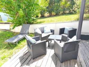 Een terras buiten met rieten meubels, waaronder stoelen en een tafel, op een houten terras.